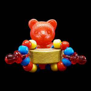 A hollow plastic bear sitting inside a chubby bagel adorned with pony beads and mini pacifiers. It's like four foot toys rolled into one! Designed for intermediate to medium birds.  Measures approx 2" by 2".